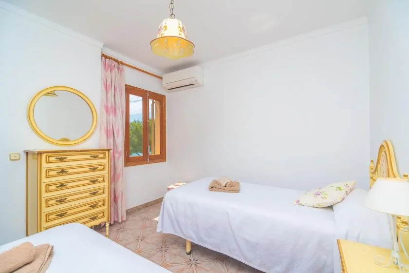 A bright bedroom with beds, a wooden dresser, and a window with floral curtains.