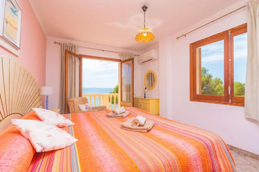 A bedroom with a colorful bedspread and windows overlooking the sea.