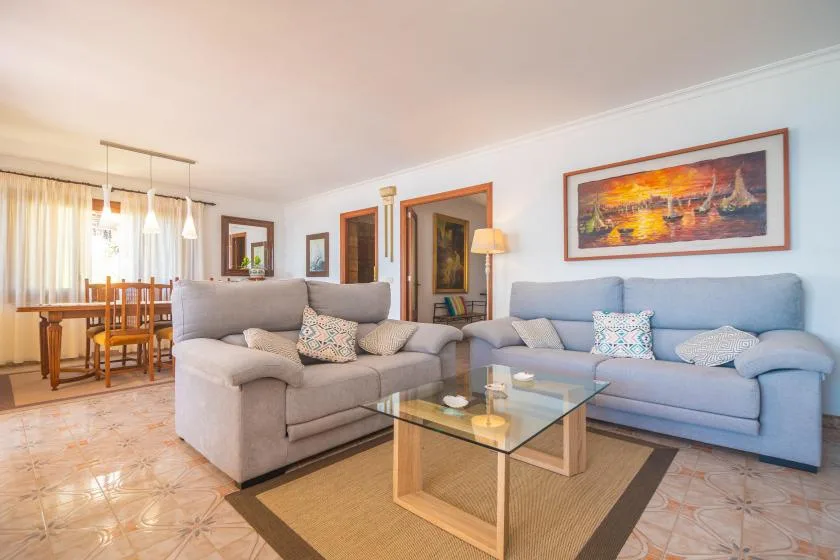A living room with seating around a glass coffee table and a dining area beyond.
