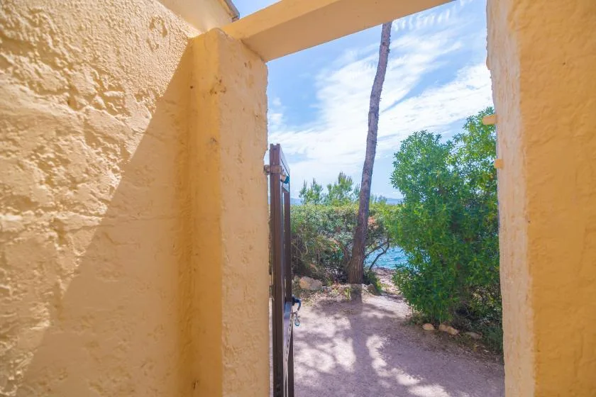 A sunlit outdoor path framed by a yellow stucco doorway, with trees beyond.