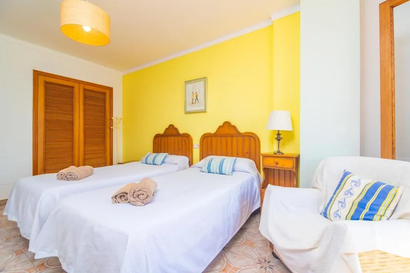 A bright bedroom with two beds, yellow walls, and a cushioned seating area.