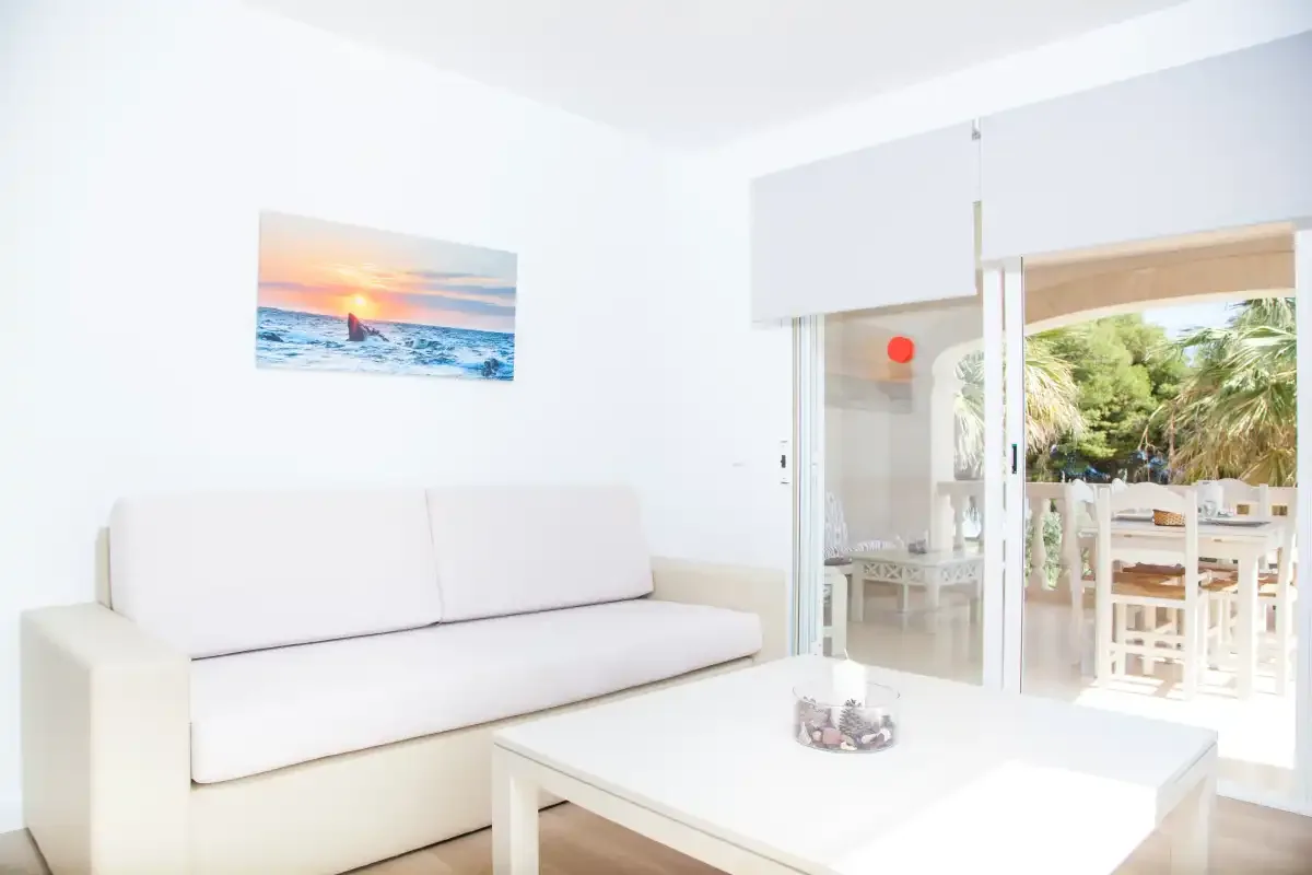 Una sala luminosa con asientos blancos y una mesa de centro junto a un patio abierto.