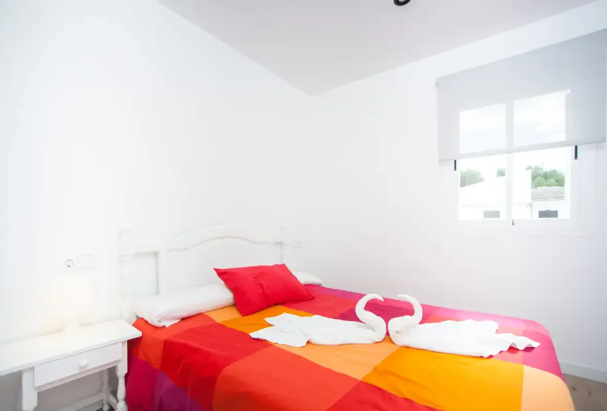 Un dormitorio luminoso con una cama cubierta con una colcha roja y naranja.