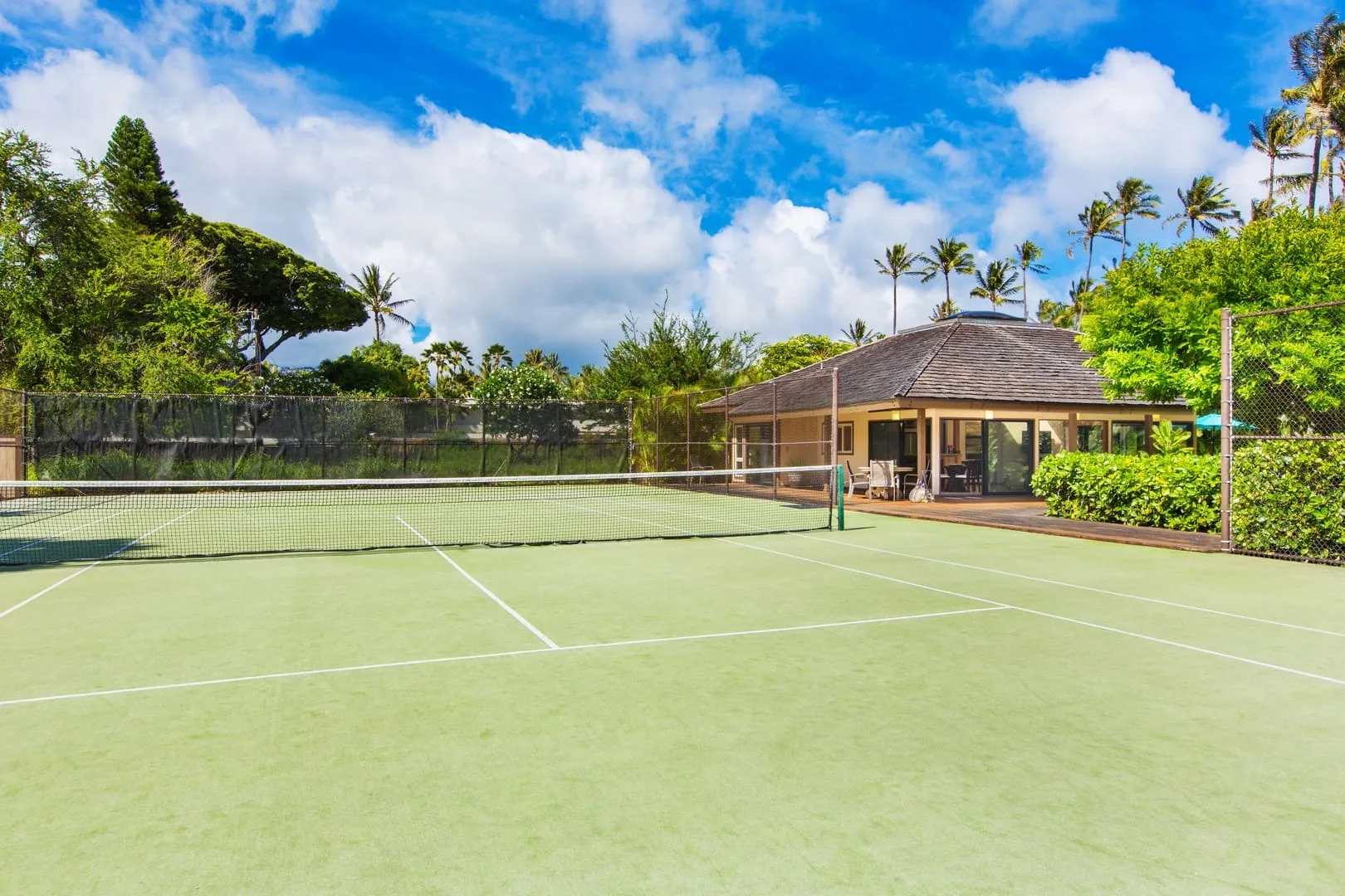 Una cancha de tenis con red está junto a un pequeño pabellón rodeado de vegetación.