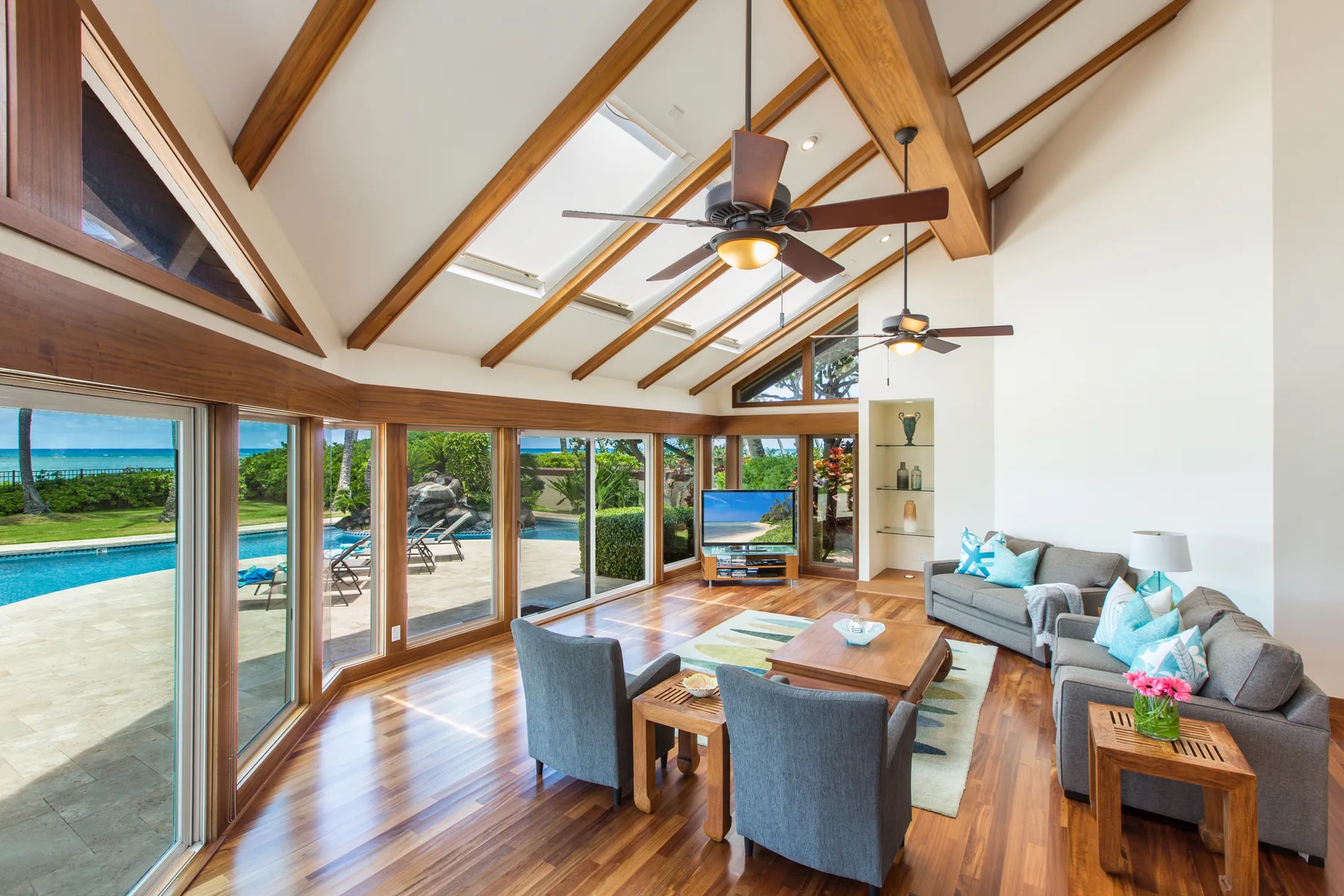 Una sala luminosa con vigas expuestas en el techo y grandes ventanas con vistas a una piscina.