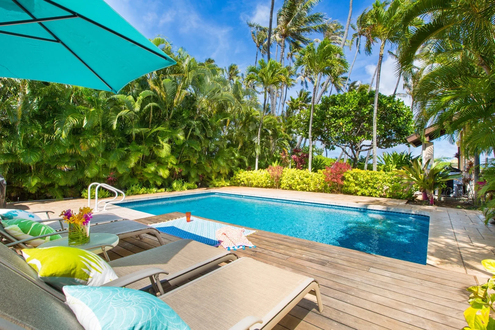 Una piscina al aire libre rodeada de vegetación tropical, con asientos reclinables en la terraza.