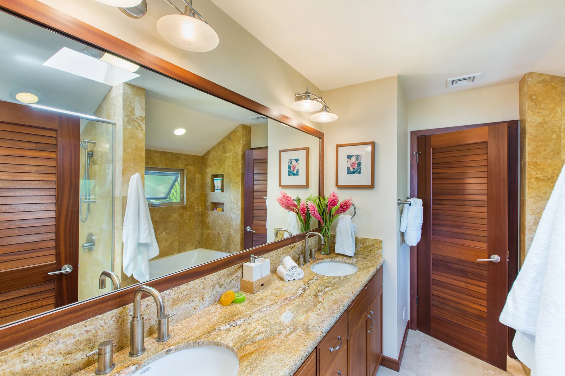 Un tocador de baño con un espejo amplio, lavabos y puertas de madera.