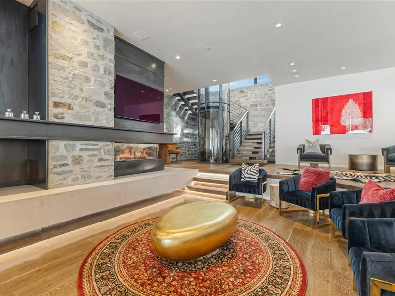 A spacious living room features a stone fireplace, seating, and a staircase.
