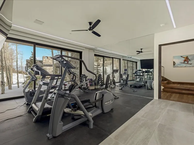 A bright gym with exercise machines beside large windows.