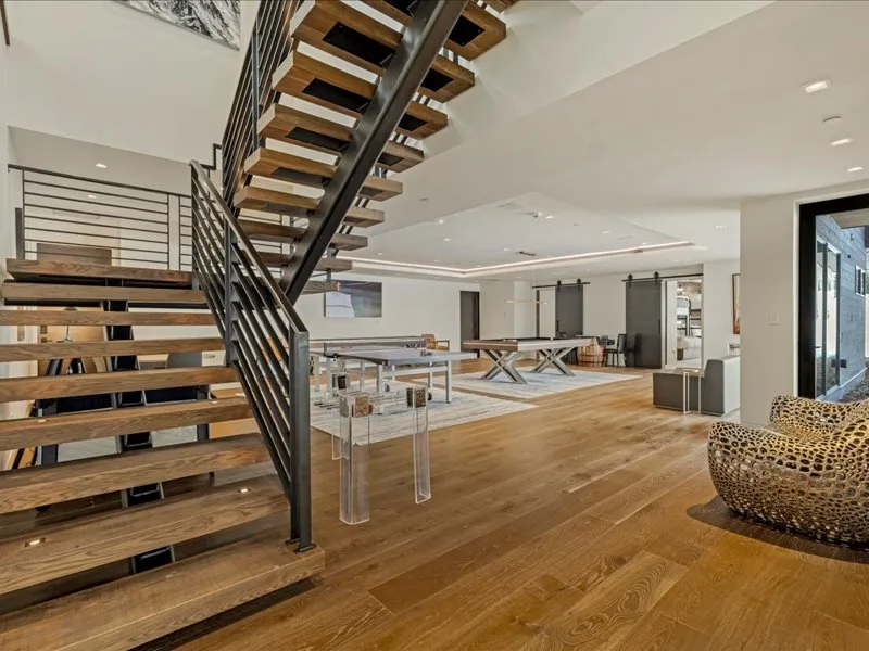 A spacious open-plan living area with a prominent staircase and wooden flooring.