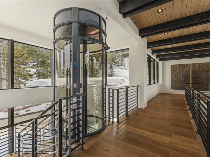A modern interior walkway surrounds a glass elevator and overlooks a snowy landscape.