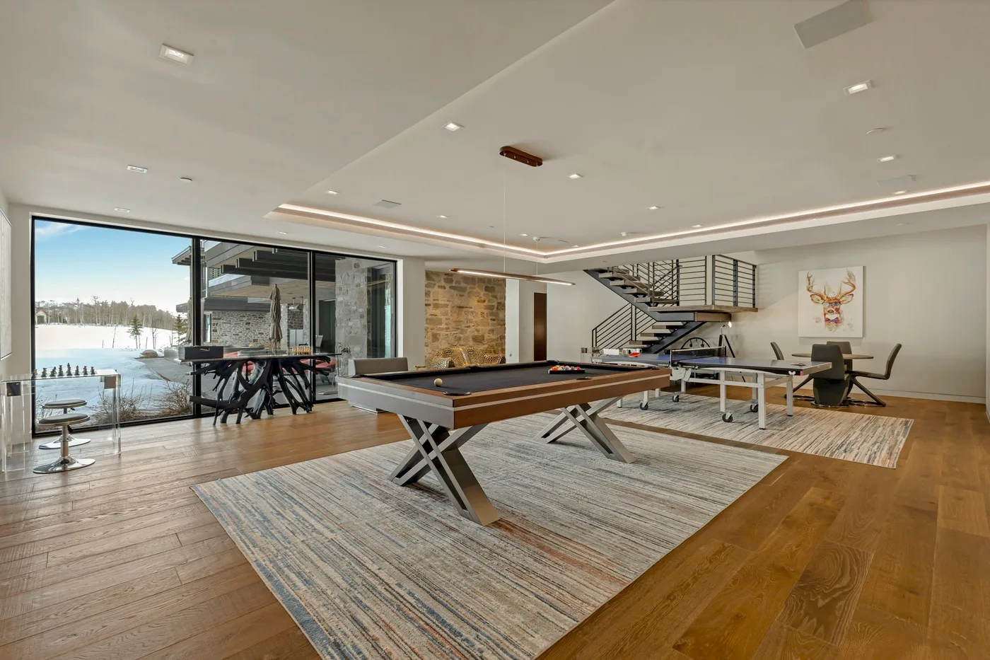 A billiards room with a pool table and dining area beside large windows.