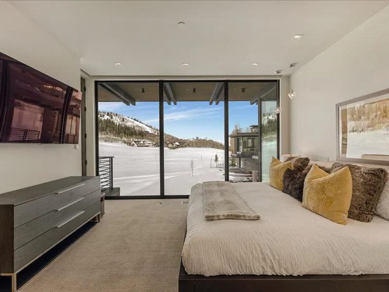 A bedroom with a bed beside large windows overlooking a snowy landscape.