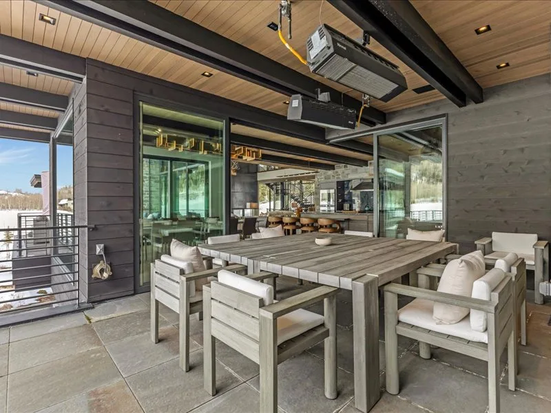 A covered outdoor dining area with a long table and surrounding seating.