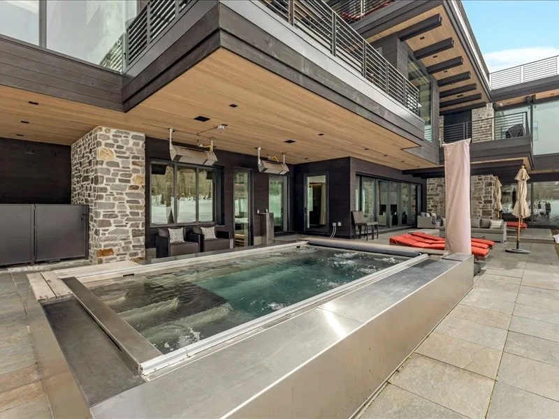 An outdoor pool sits beside a modern building with stone walls and a wooden overhang.
