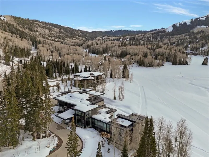 A modern mountain lodge sits beside a snowy clearing surrounded by forested hills.