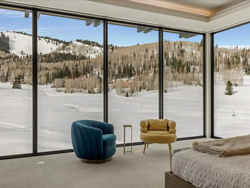 A bedroom seating area overlooks a snowy landscape through large windows.