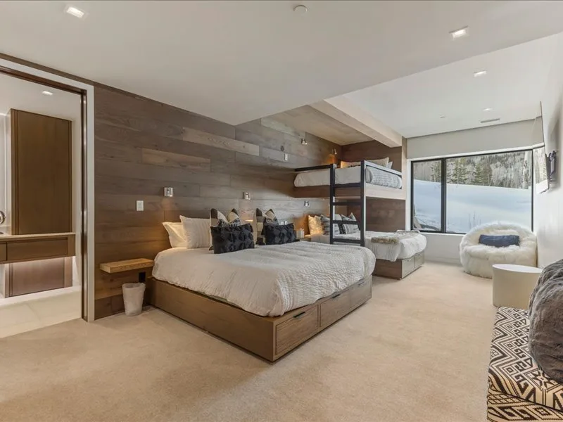 A modern bedroom with a large bed, a bunk bed, and a wide window.