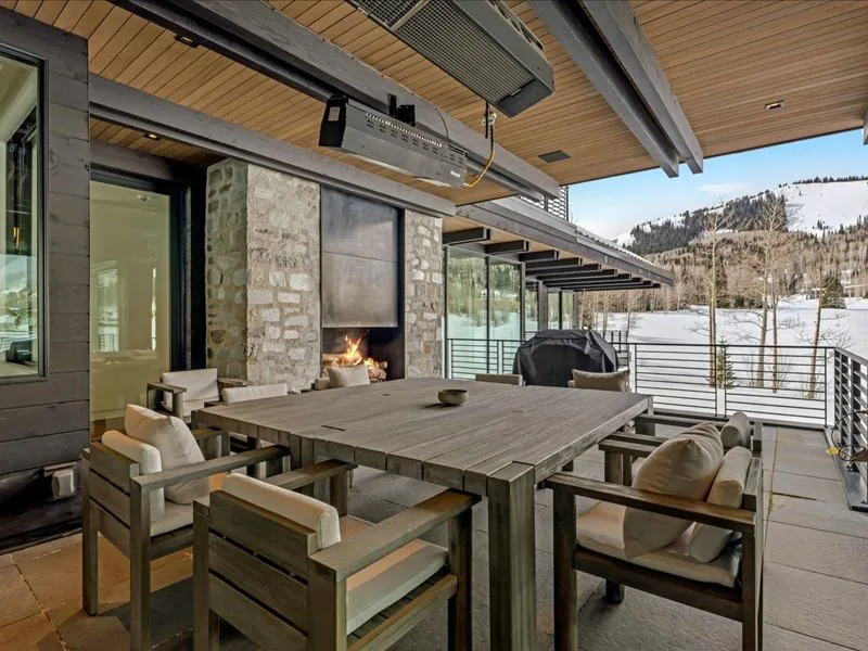 A covered outdoor dining area with a large table and chairs overlooks a snowy landscape.