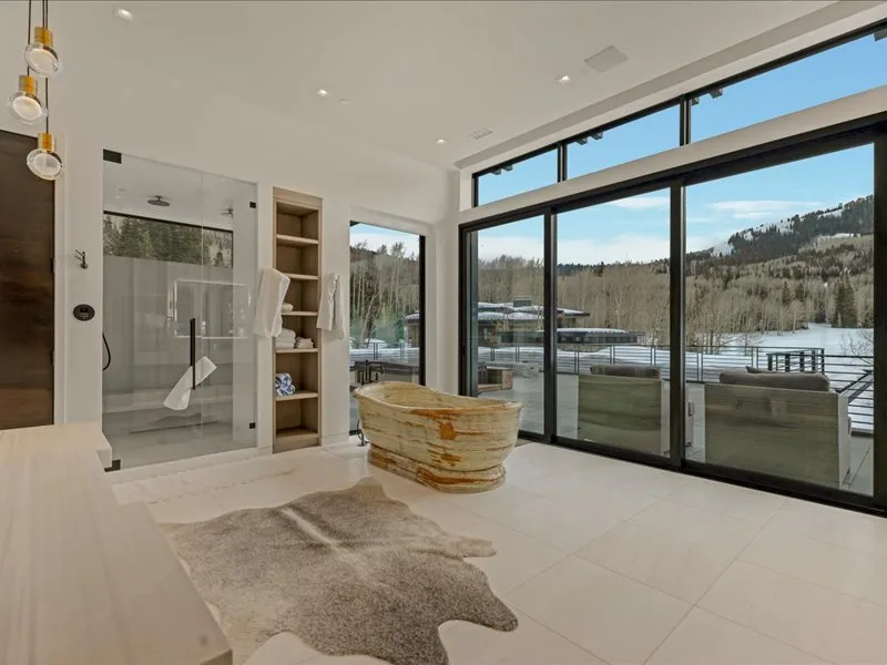 A bright bathroom with a freestanding bathtub beside large windows overlooking the landscape.