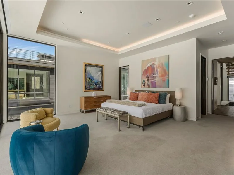 A bright bedroom with a bed, colorful artwork, and a large window.