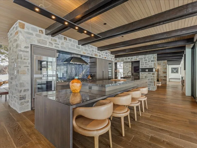 A spacious kitchen with a long island and seating beneath exposed dark beams.