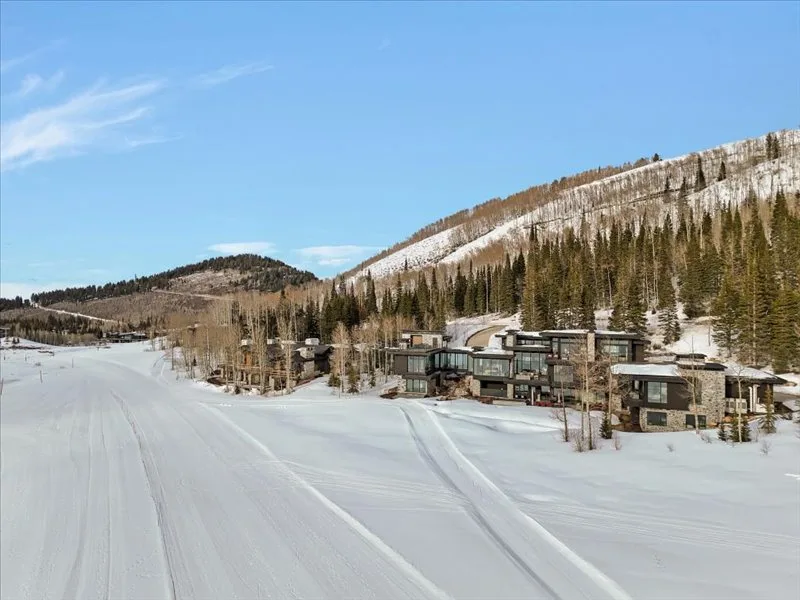 A snowy mountain landscape with evergreen trees and modern buildings along a ski slope.