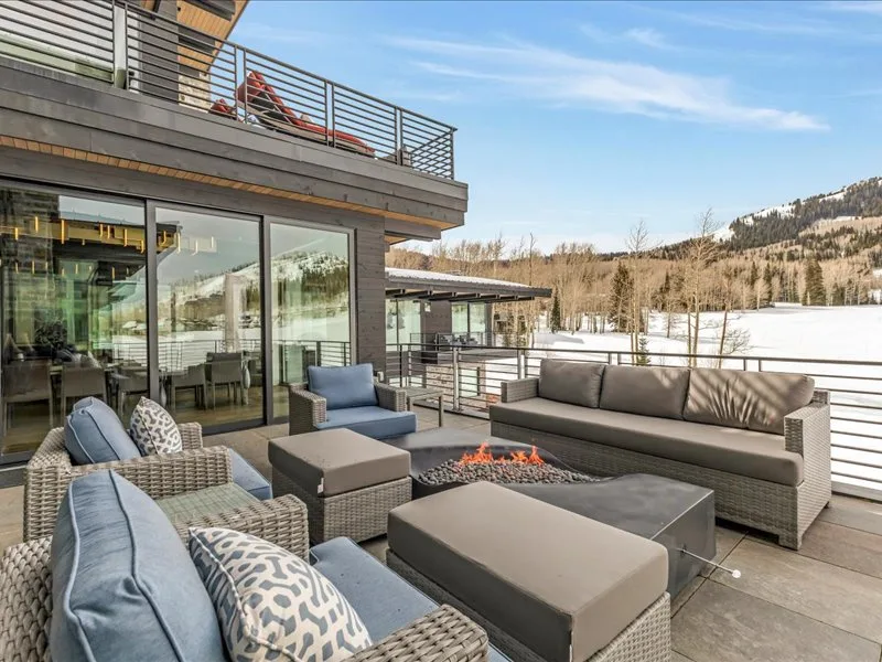 A furnished outdoor terrace with seating and a fire pit overlooks a snowy landscape.
