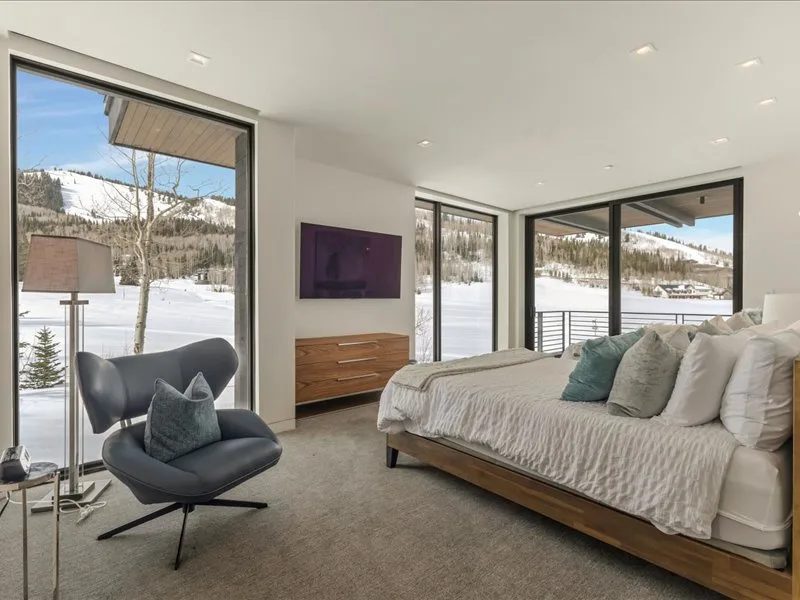 A bedroom with a bed and seating beside large windows overlooking a snowy landscape.
