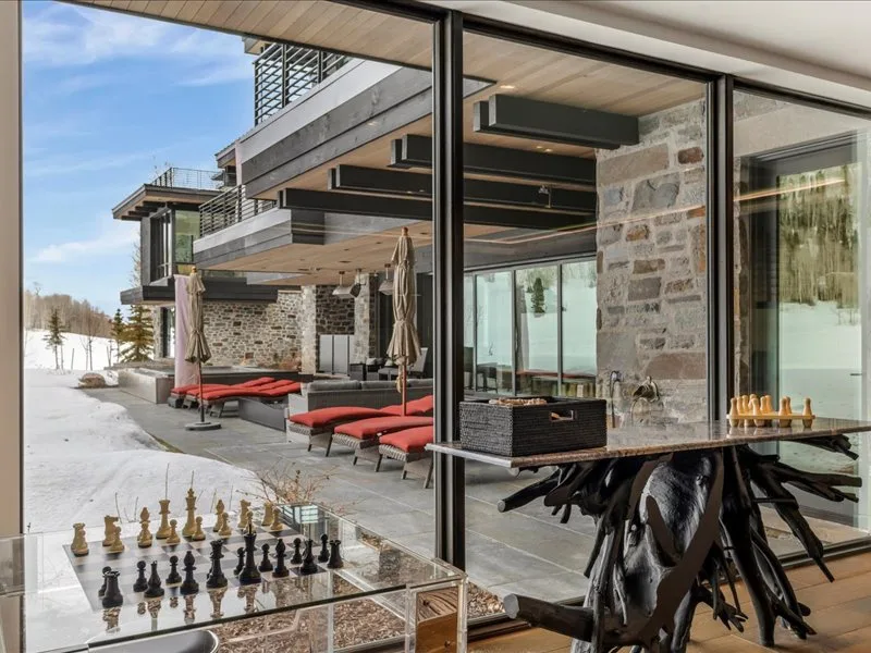 A modern patio seating area opens onto a snowy landscape, with a chess set in the foreground.