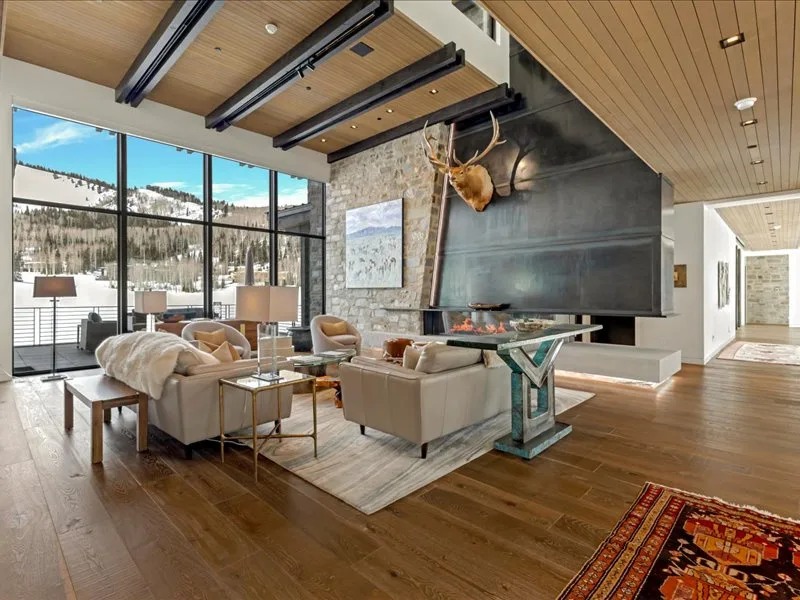 A spacious living room with seating arranged around a fireplace and large windows.