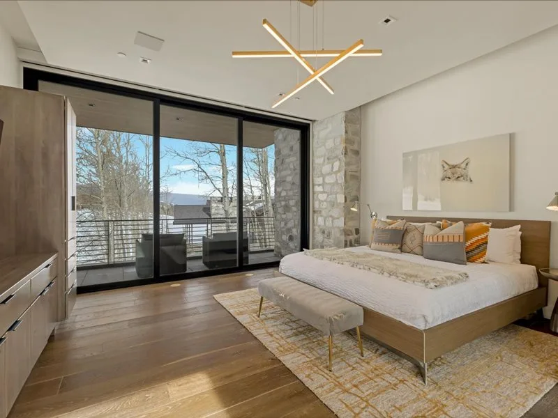 A bright bedroom with a large bed beside floor-to-ceiling windows overlooking a balcony.