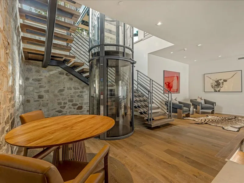 A modern living area with a glass elevator, staircase, and seating.