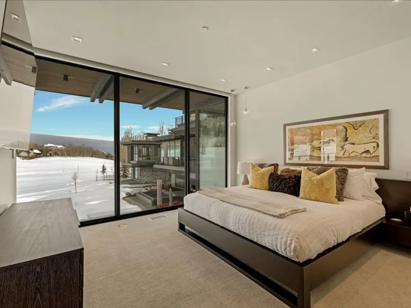 A bedroom with a large bed beside floor-to-ceiling windows overlooking a snowy landscape.