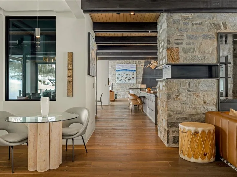 An open-plan dining and kitchen area features a glass dining table and stone walls.