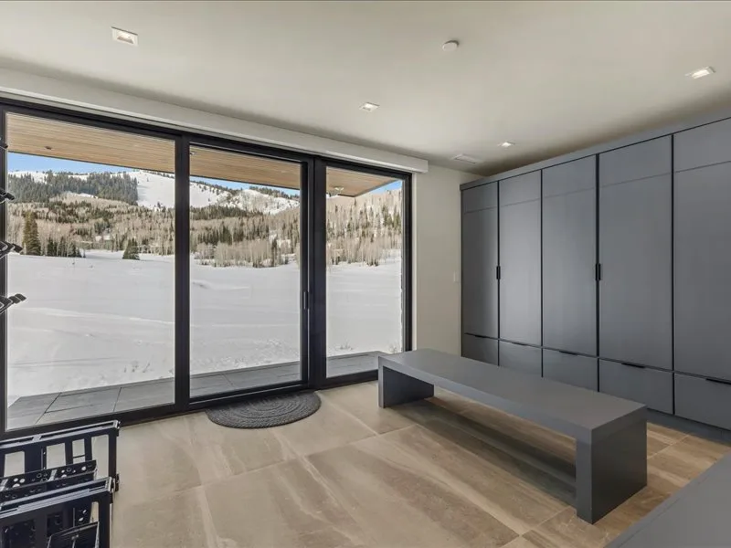 A modern interior room opens onto a snowy landscape through large glass doors.
