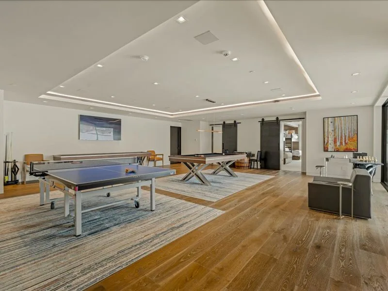 A spacious recreation room with a ping-pong table and wooden flooring.