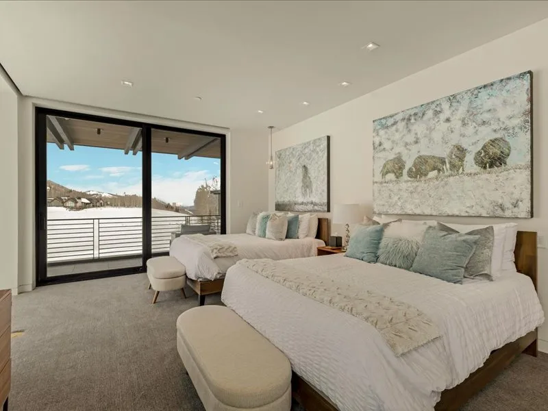 A bright bedroom with two beds, pale bedding, and sliding glass doors.