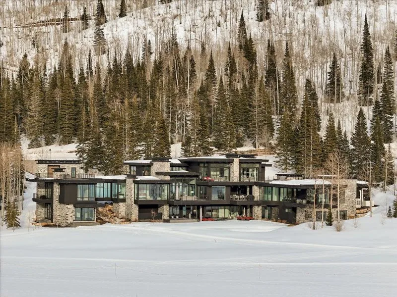 A modern building stands beside a snowy slope and a forest of evergreen trees.