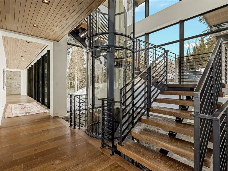 A bright interior stairway beside a glass elevator, with large windows.