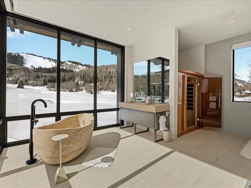 A modern bathroom features a freestanding bathtub beside large windows overlooking a snowy landscape.
