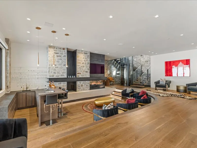 A spacious modern lounge has a sunken seating area, stone fireplace, and staircase.