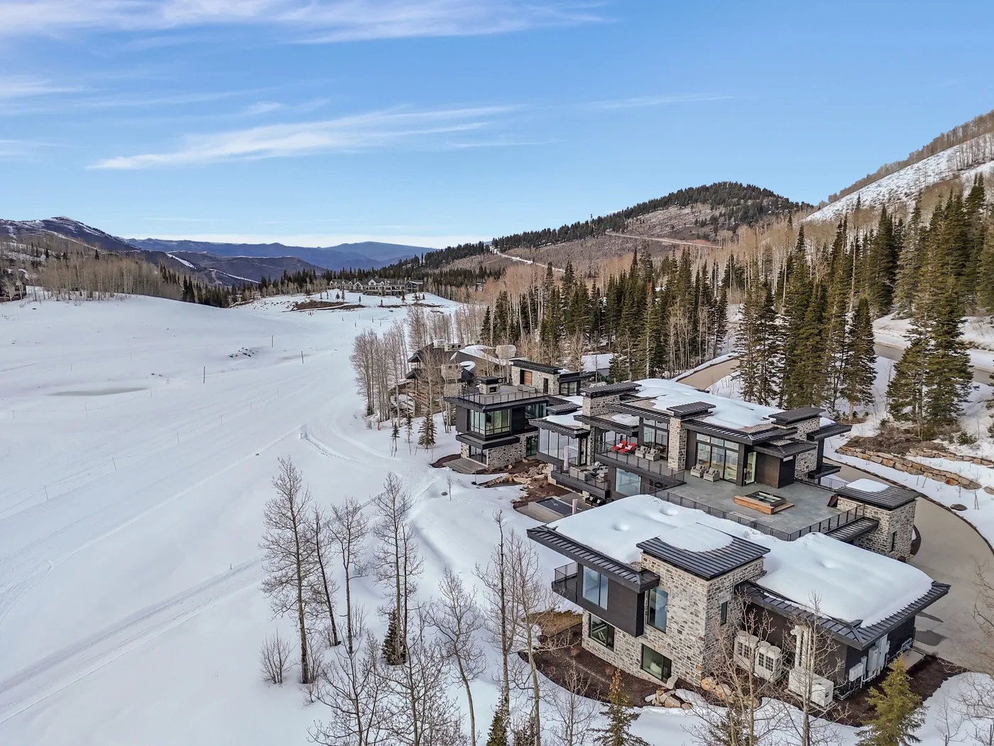 Modern buildings sit beside a snow-covered open field, with wooded hills in the distance.