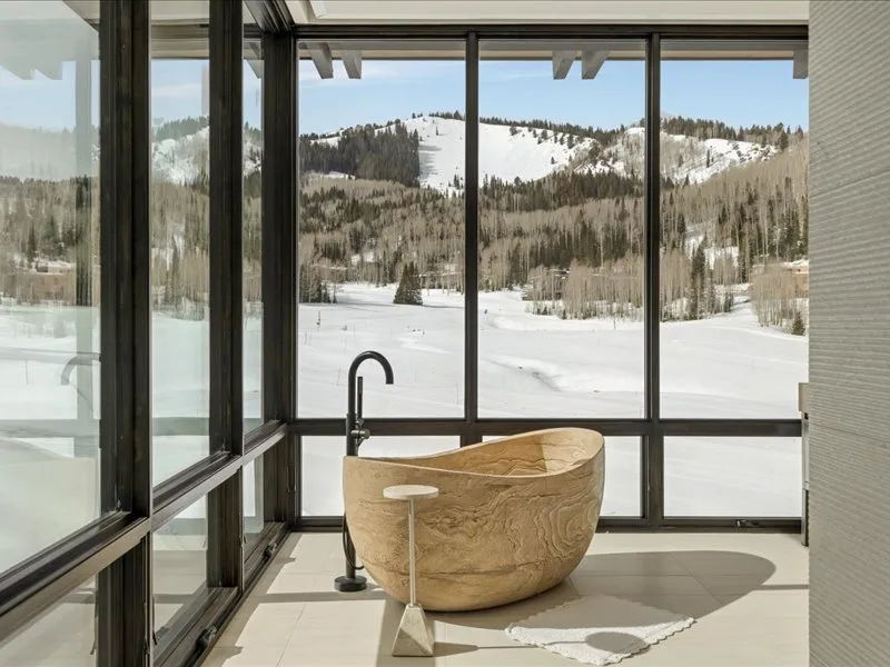 A freestanding bathtub sits beside large windows overlooking a snowy landscape.