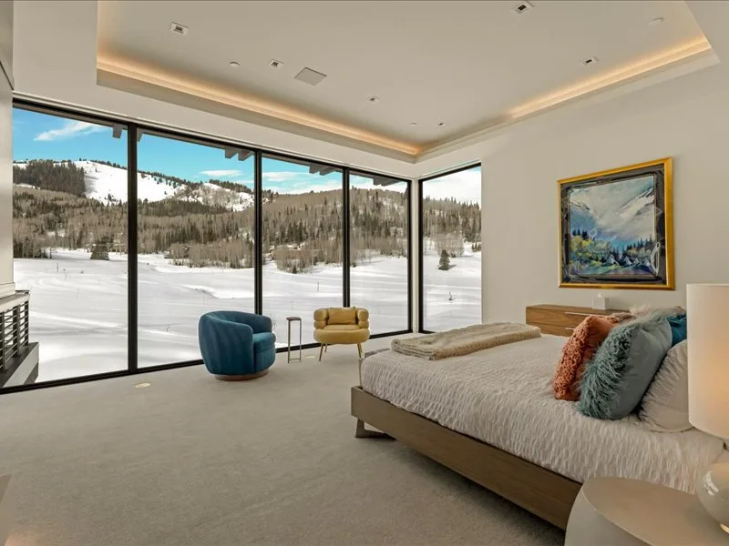 A bright bedroom with a bed and large windows overlooking a snowy landscape.