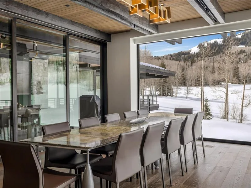A dining area with a long table and large windows overlooking a snowy landscape.