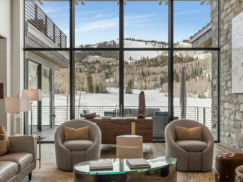 A modern living room with cushioned seating and large windows overlooking a snowy landscape.