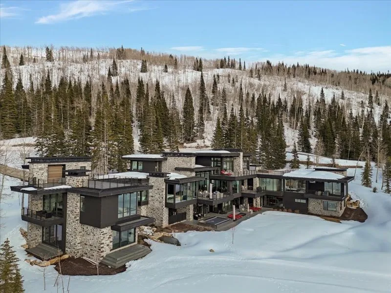 A modern multi-wing building sits in a snowy, forested mountain landscape.