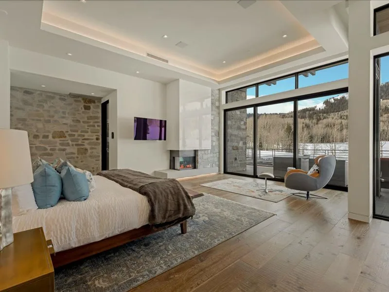 A bright bedroom opens onto a glass-walled sitting area with views of the hills.