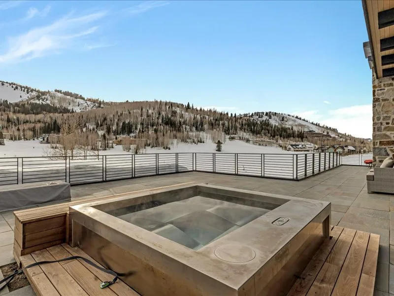 An outdoor hot tub sits on a wooden deck overlooking a snowy hillside.